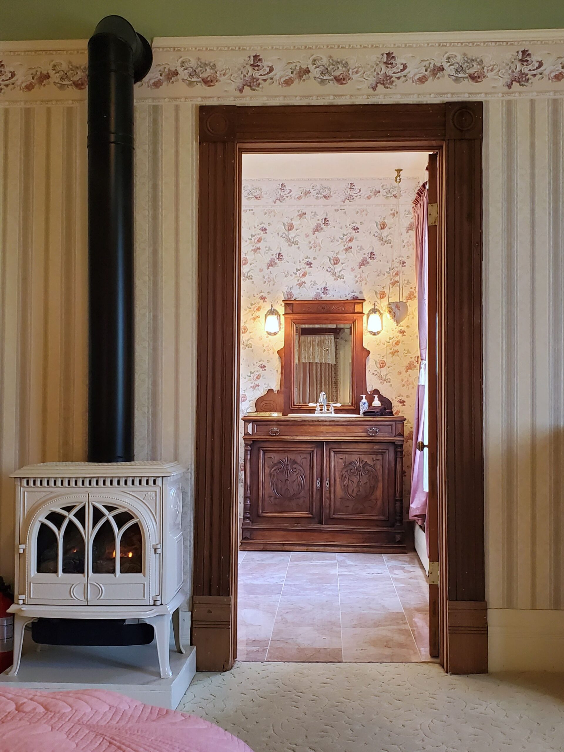 View from the Victoria Suite through the doorway to the antique dresser vanity bathroom, with propane fireplace in the foreground