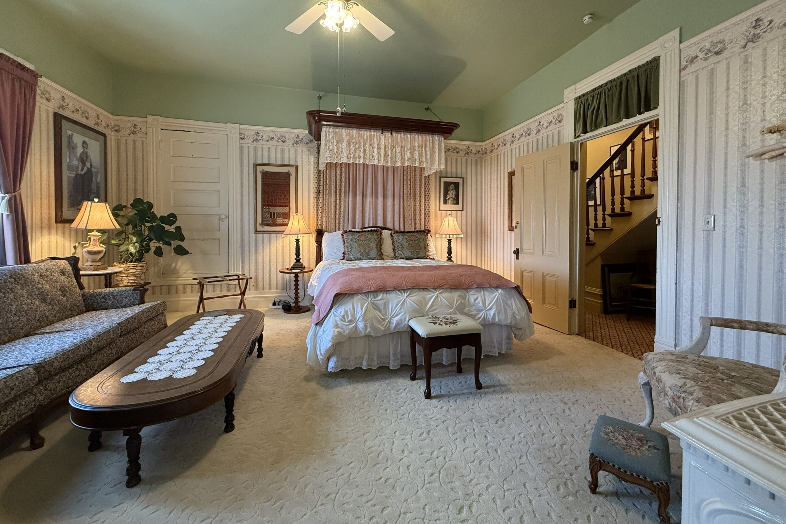 Half-tester bed draped in lace, sofa and coffee table at least, door to hallway at right